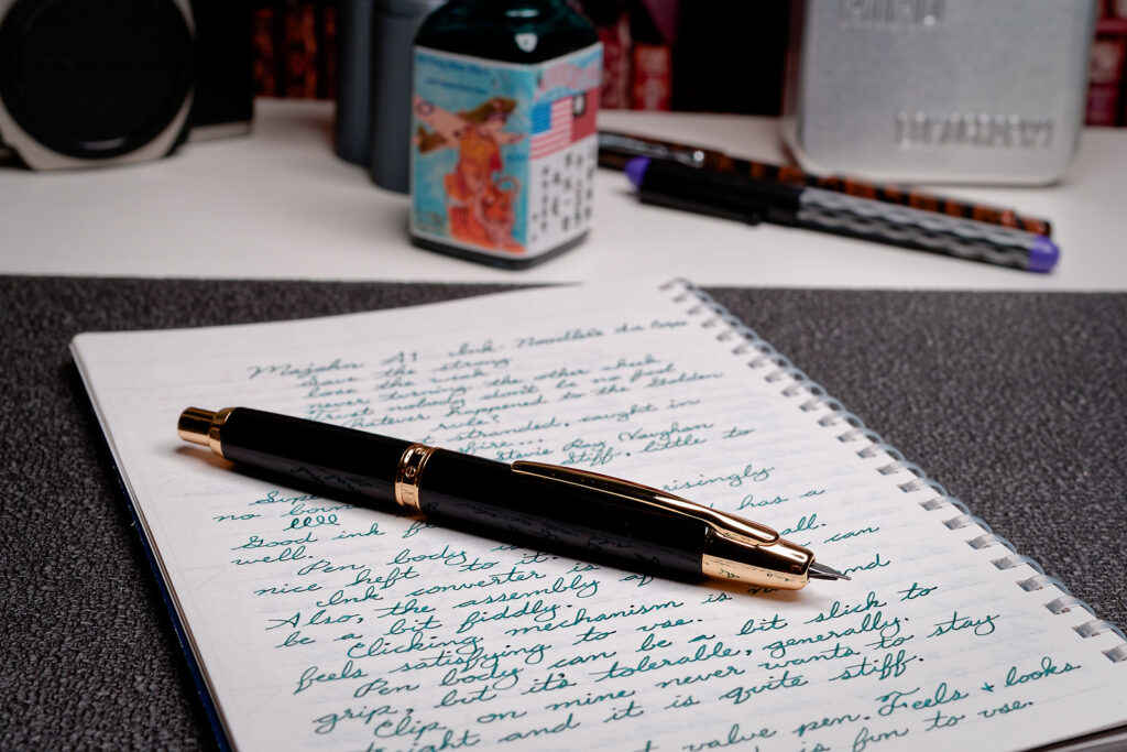 A photo of a Majohn A1 on a notebook with a writing sample. The fountain pen has it's nib in the writing position. 