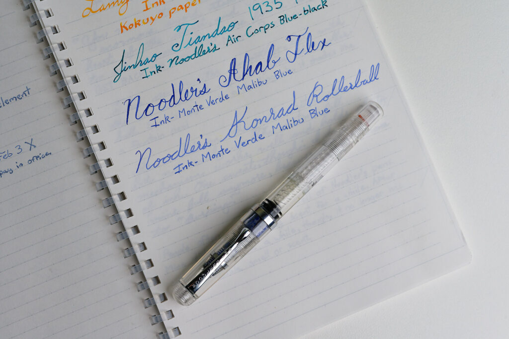 A Noodler's Konrad Rollerball pen on top of a notebook with the pen name written in blue ink.