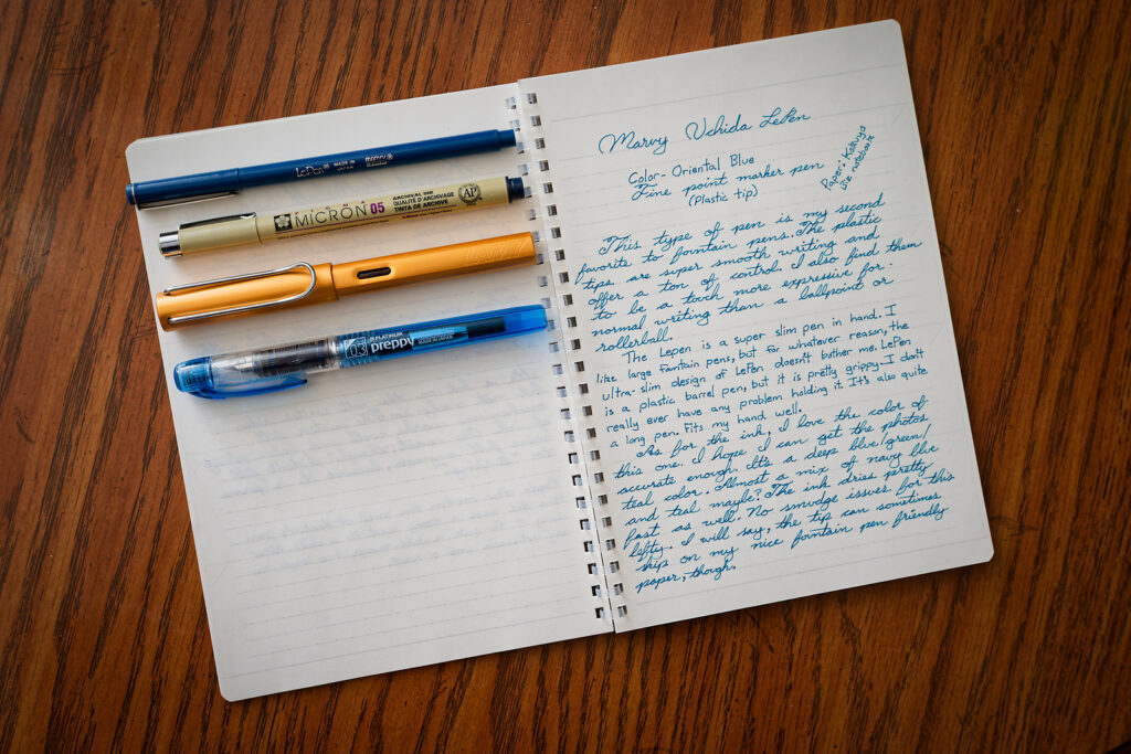 A photo of an open notebook with a Marvy Le Pen, Pigma Micron, Lamy Al-Star, and a Platinum Preppy placed near each other as a size comparison.