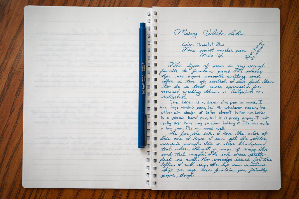 A writing sample done in a Kokuyo Biz Notebook with an Oriental Blue Marvy Le Pen placed upon it. 