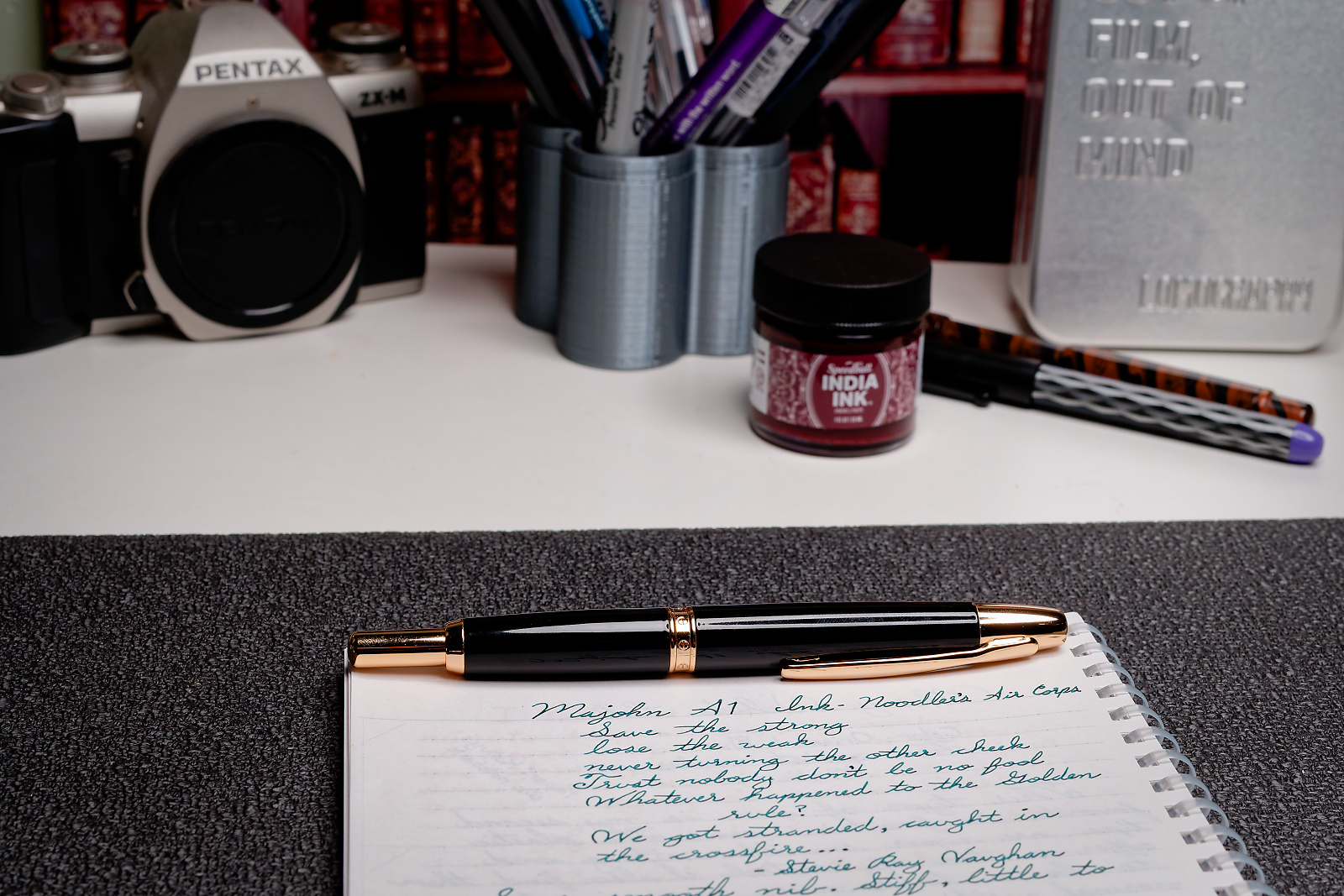 A photo of a desktop scene. A Majohn A1 fountain pen is sitting on a notebook with writing samples from the pen below it.