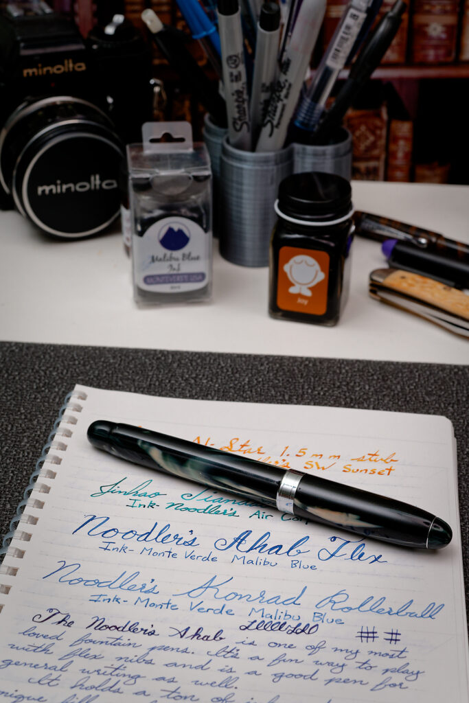 A photo of the Noodler's Ahab flex fountain pen with the cap on. It's placed on a notebook containing writing samples from the pen.
