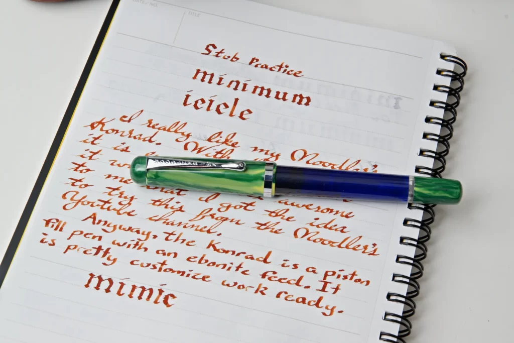 A Noodler's Konrad Thule fountain pen laying on a notebook featuring writing samples from the pen.