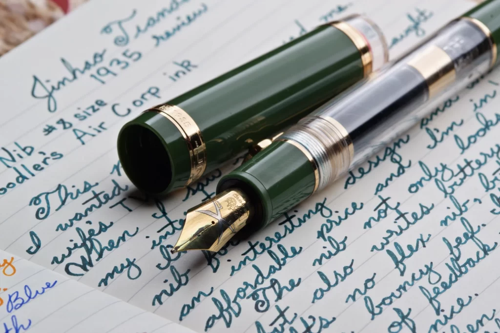 A Jinhao Tiandao 1935 fountain pen with its cap off. The nib is facing the camera and the cap is placed above the pen.
