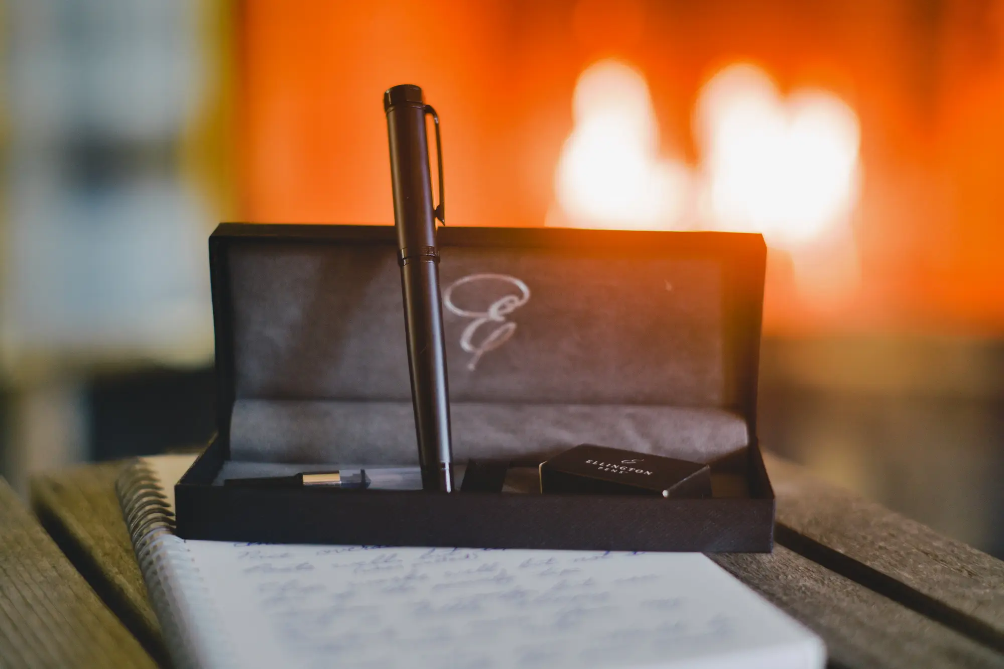 A matte black Ellington Stealth fountain pen stood up out of the Ellington pen box that the pen came in. There is a fire out of focus in the background