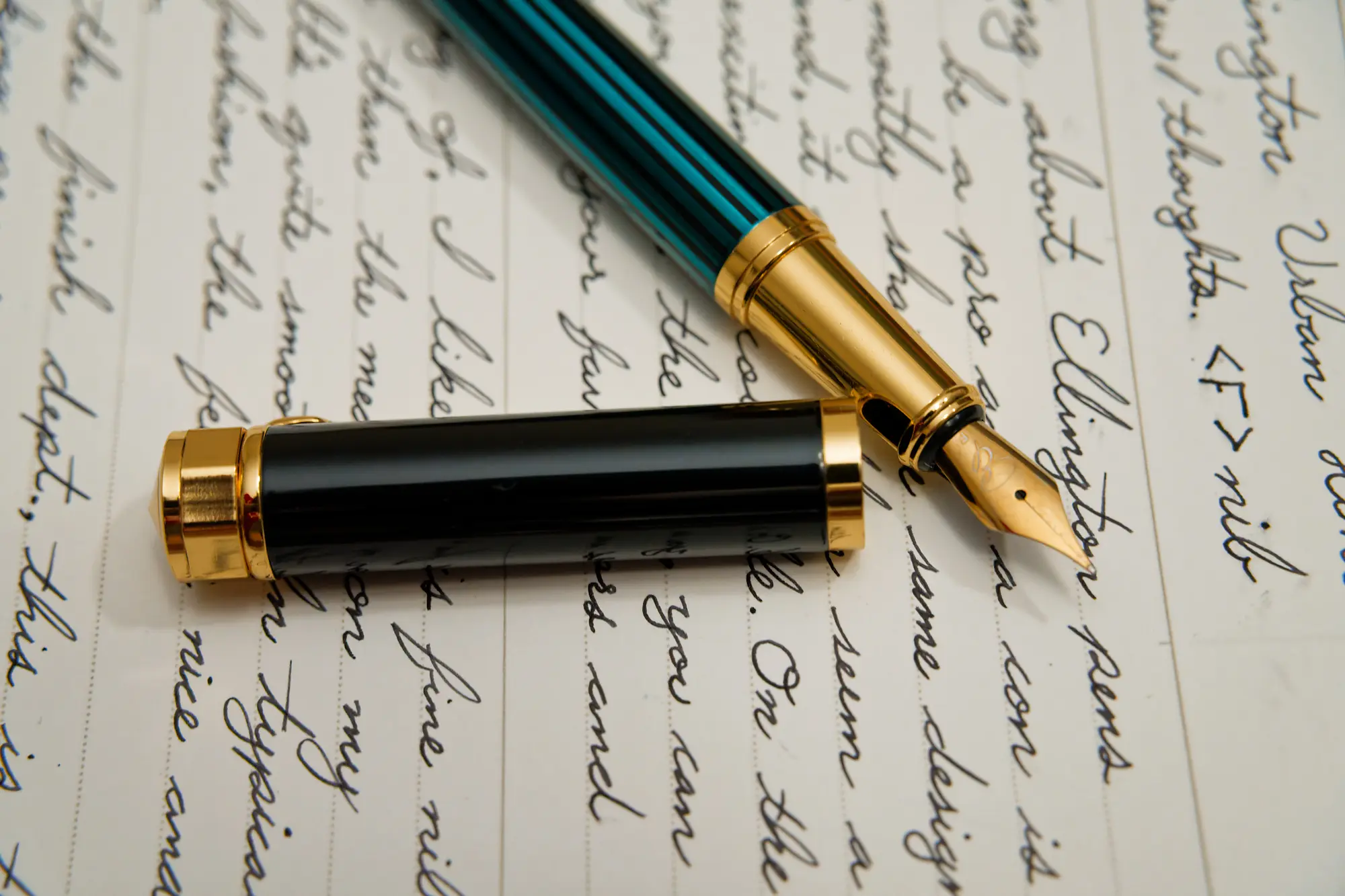 This photo show an Ellington Pens fountain pen sitting on a lined piece of paper. The pen is the Urban Hunter model, featuring a gold colored grip section, clip, nib, can cap bands. The body is a deep teal/green color with black, vertical stripes.